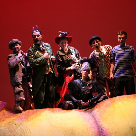 The ensemble from James & the Giant Peach pose on stage in their costumes behind the giant peach set piece.