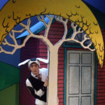 Al Kroeten in Go Dogs Go, dressed in a black and white dog costume and peeking out from behind a cartoon tree