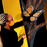 Tamia Renée as the Monarch butterfly in HOW TO BUILD AN ARK. PHOTO DESCRIPTION: A female actor wearing a black costume and orange face mask holds up an orange and black Monarch butterfly puppet.