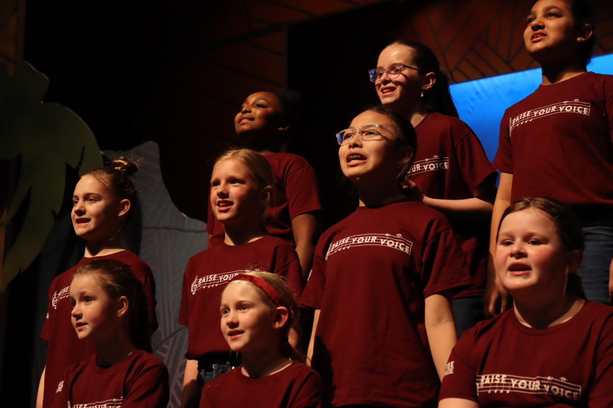A diverse group of young students performing a vocal music number in matching t-shirts.
