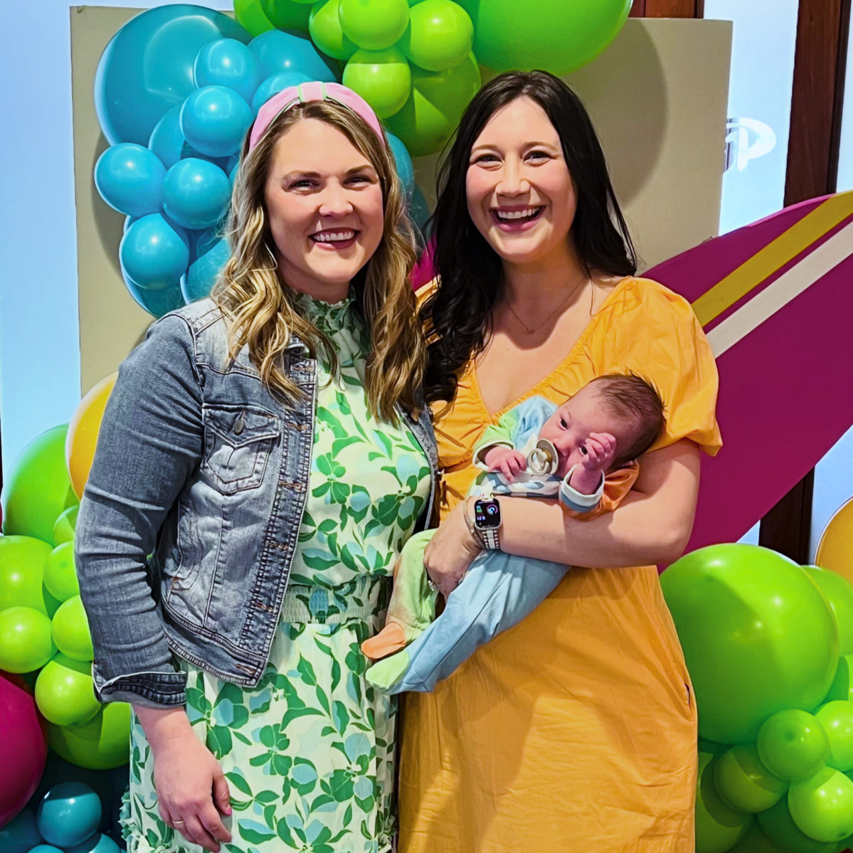 Two Rose Guild Members smiling at Rockin' Rosie 2024. The woman on the right is holding a child in her arms.